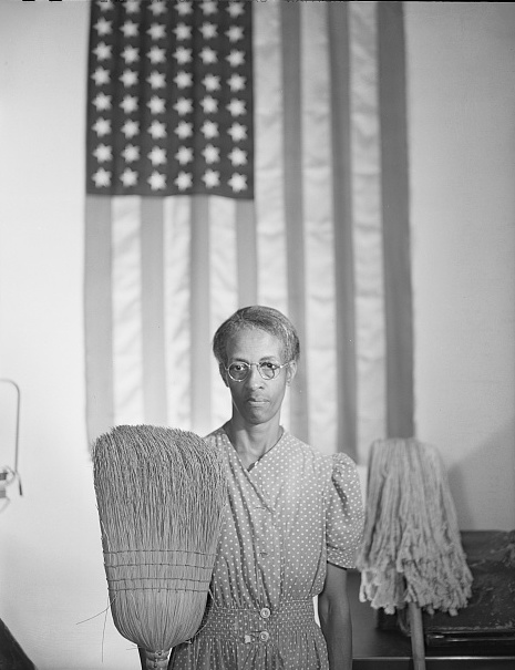woman holding broom and mop in front of American flag