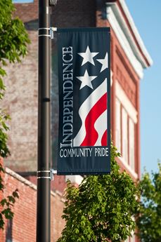 A vertical blue banner with white stars and red and white stripes reading "Independence: Community Pride"