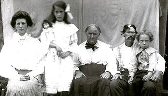 Black and white. A family of five is seated in front of a plain backdrop.