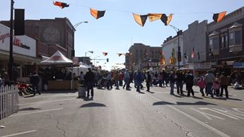 A city street is filled with people celebrating a festival with a banner is overhead.