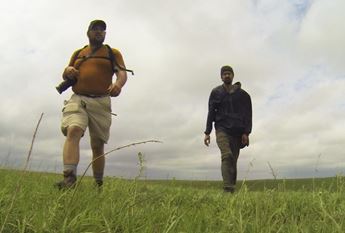 Two men walking through prairie landscape