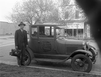 historic photo of man standing by automobile