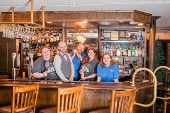 People stand behind an old-fashioned hotel bar.