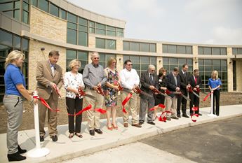 A line of individuals participates in a ribbon cutting for a new health care facility.