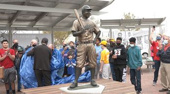 Jackie Robinson statue holding a bat against his shoulder at Wichita's McAdams Park is surrounded by onlookers.