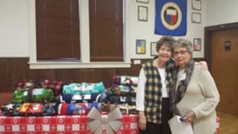 Two women stand in front of a table of blankets