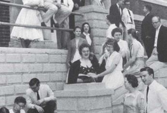 students sitting outside of a college building 1950s